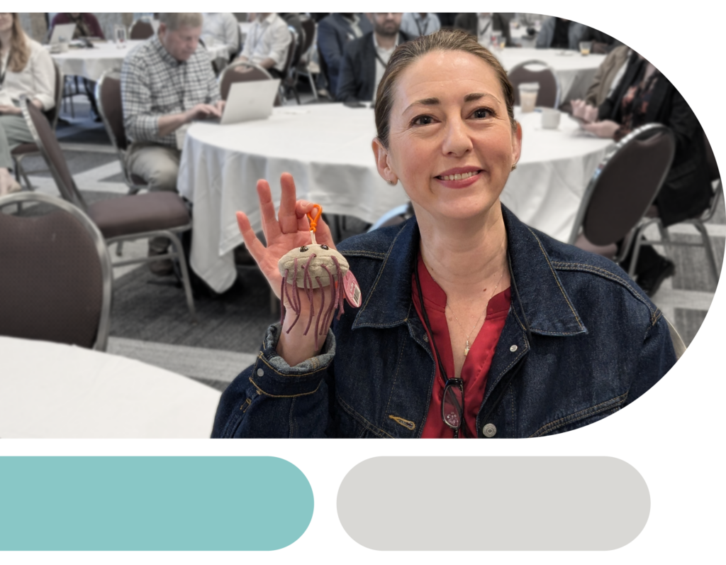 Conference attendee smiling and holding up a stuffed toy keychain that looks like a microbe